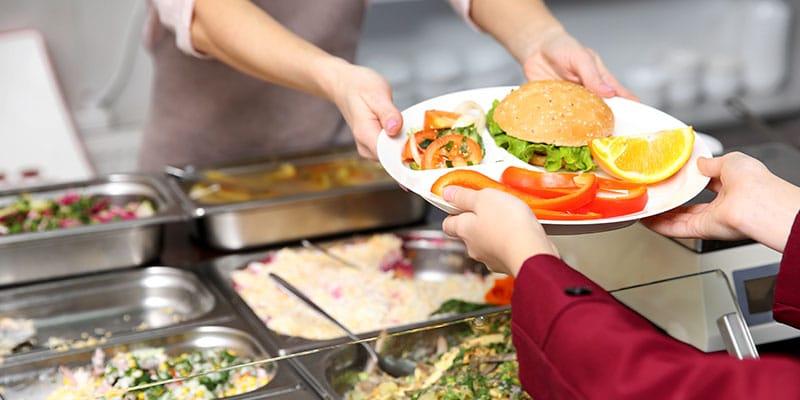Dinner server handing tray of food to child in school