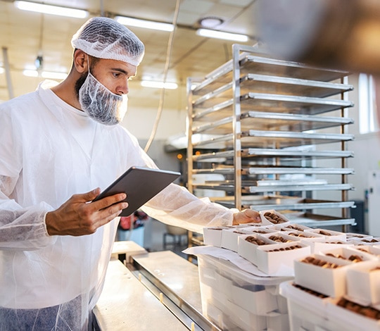 A food inspector in a sterile white uniform is holding the tablet and looking at collected cookies. Food check is important if we want quality and healthy food.