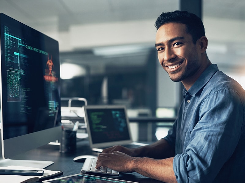 Portrait, man and smile of programmer on computer in office workplace at night. IT, face and male coder or person programming, coding and writing for software development or information technology.