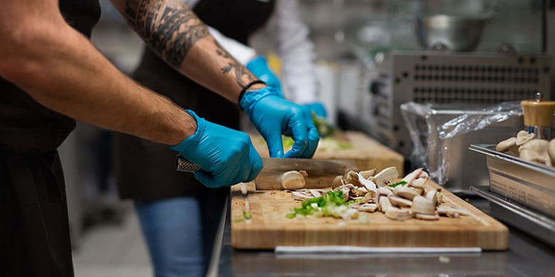 chef with gloves cutting vegetables indoors in restaurant kitchen.