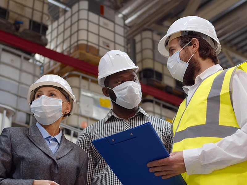Diverse warehouse inspectors wearing safety mask discussing distribution plan on clipboard