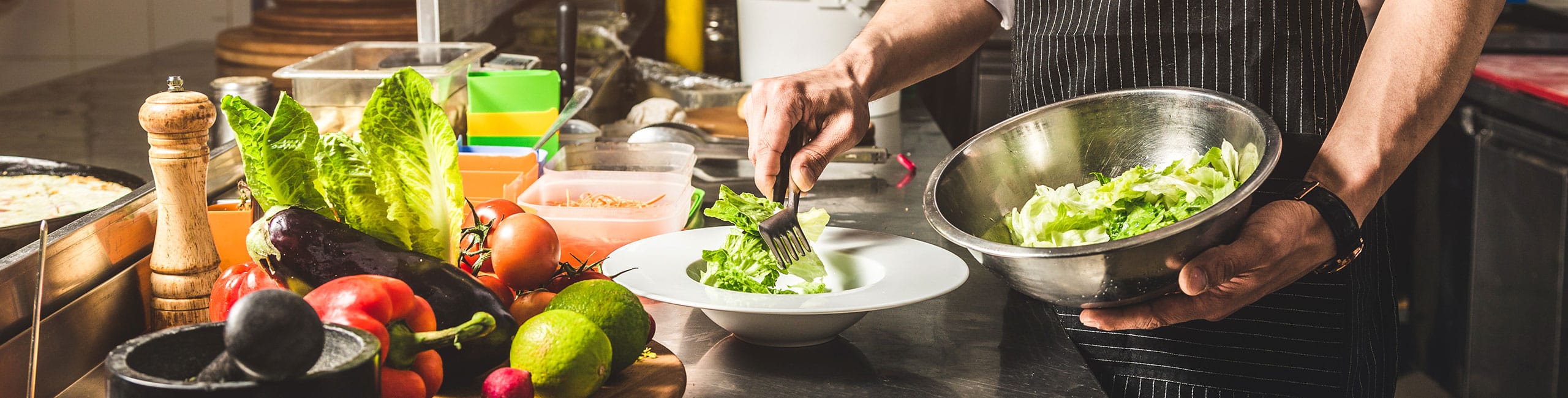 Professional chef cooking in the kitchen restaurant at the hotel, preparing dinner. A cook in an apron makes a salad of vegetables and pizza.